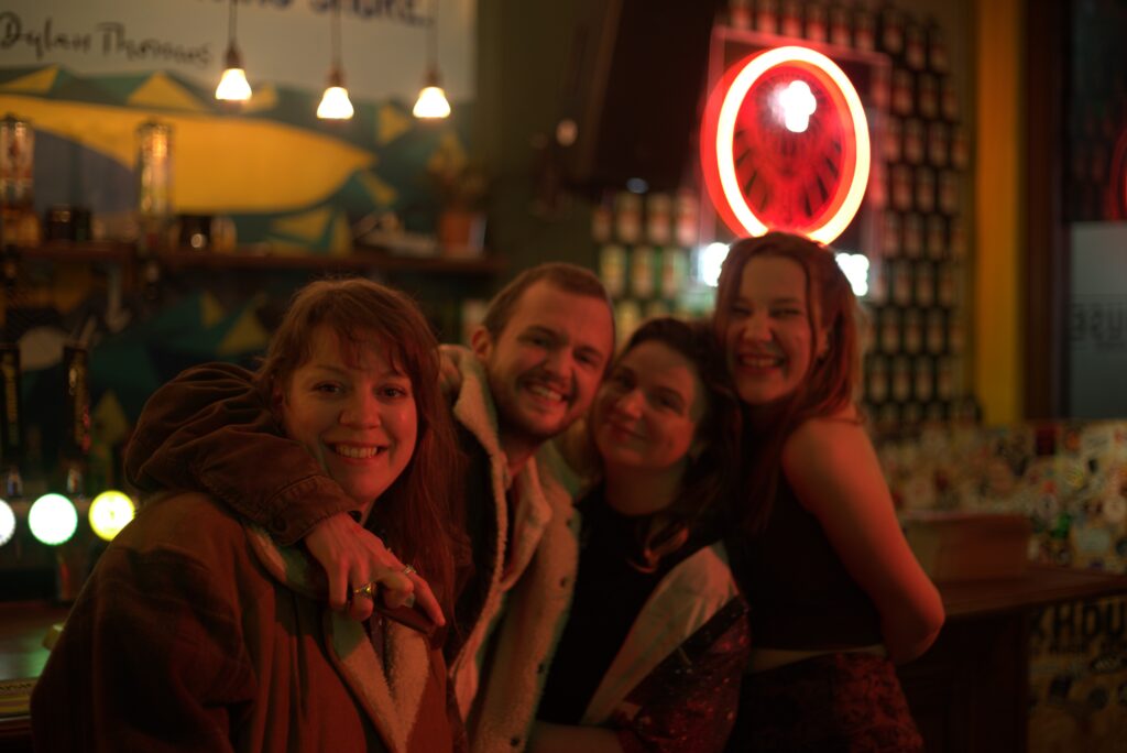A group of four people hugging and smiling enthusiastically at the camera in Bunkhouse bar.