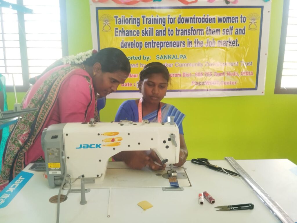 Two women by a sewing machine getting some tailoring training in Mugaiyur.